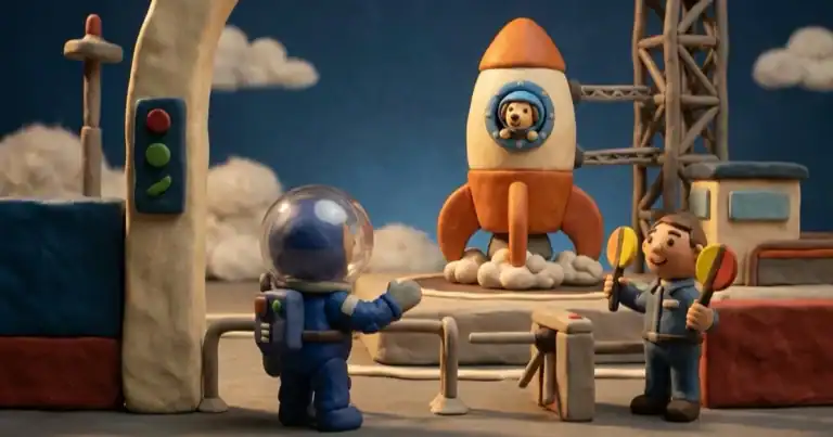 Claymation scene: a blue-helmeted astronaut waves near a rocket on a launch pad while two figures with maracas look on.